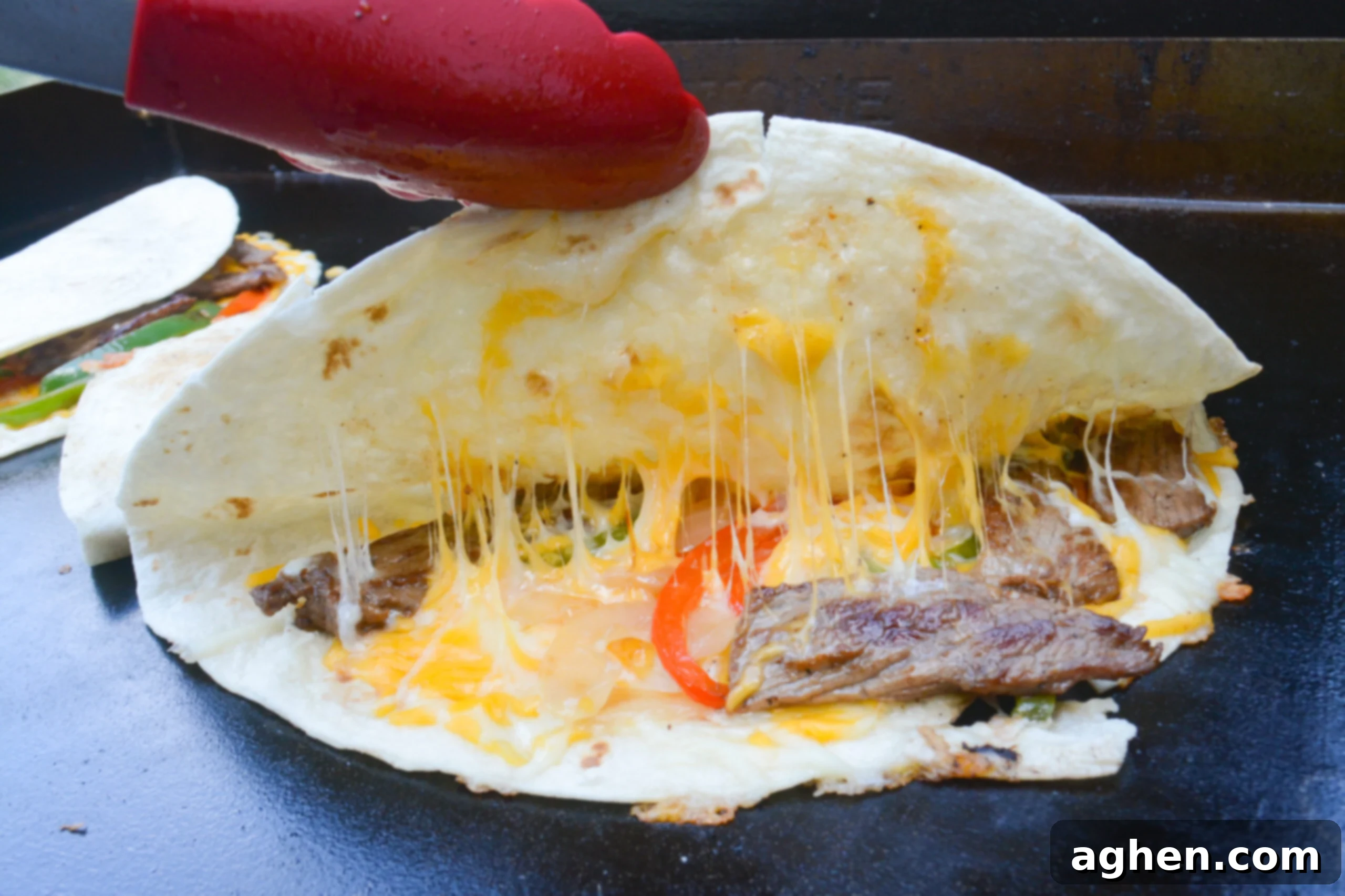 Blackstone Steak Quesadillas So Good They're Eaten Off the Griddle 9 steak quesadilla on blackstone griddle folded, but pulled up with tongs to show the melted cheese inside.