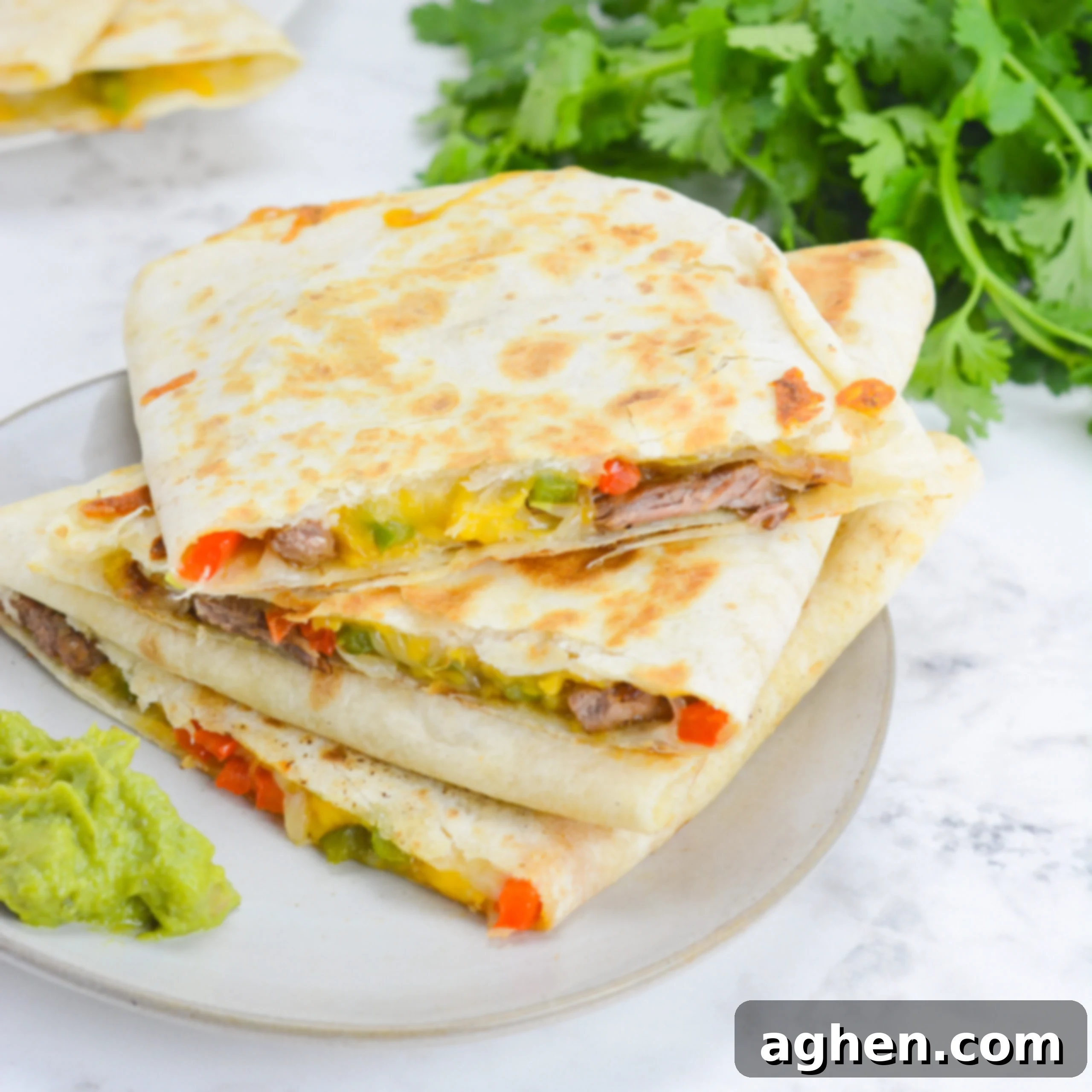 Blackstone Steak Quesadillas So Good They're Eaten Off the Griddle 10 stacked blackstone quesadillas on a white plate with a side of guacamole. cilantro rests in the background.