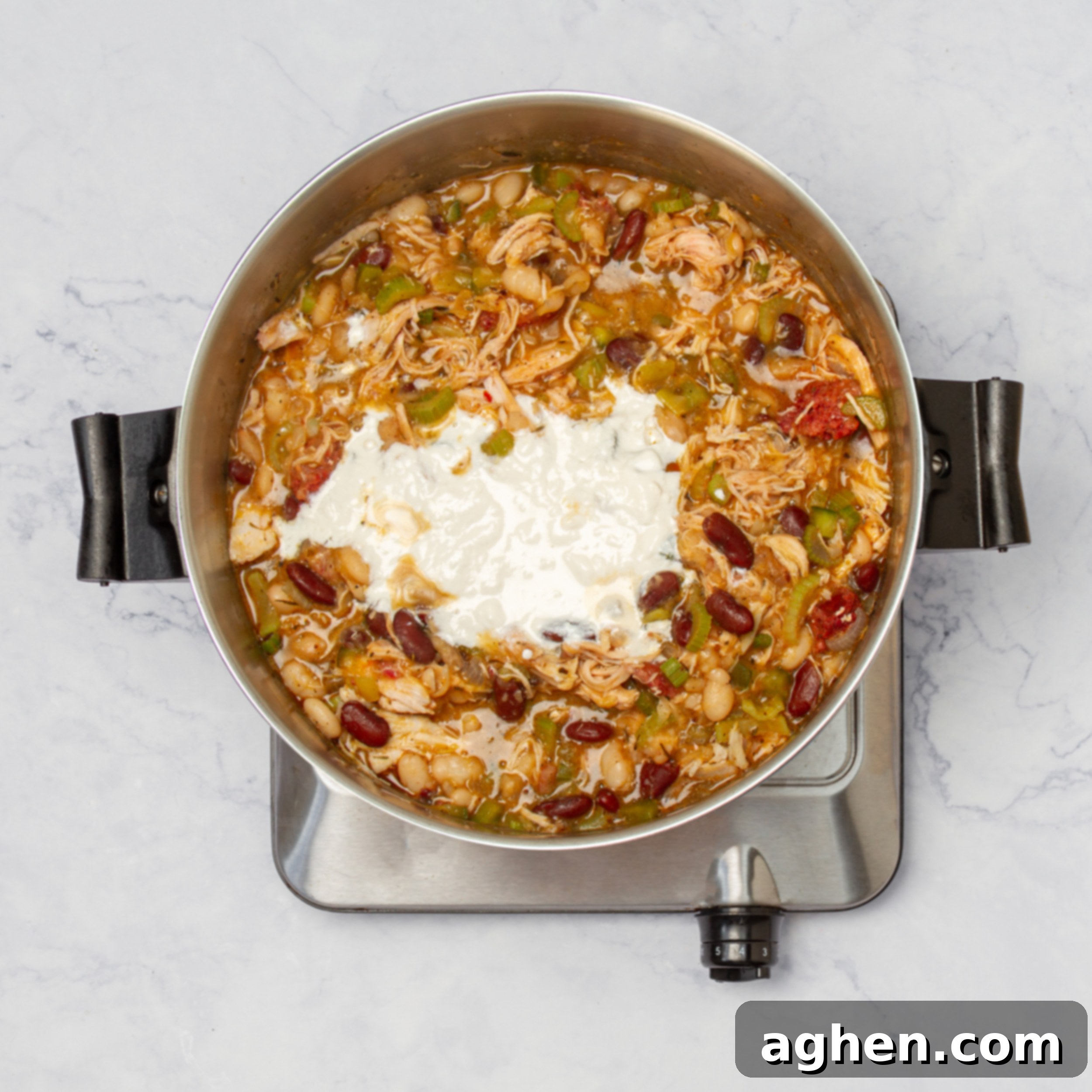 Creamy Cajun Chicken Chili 7 Shredded chicken, white beans, and a sprinkle of cheese being added to the simmering pot of chili on the stove, enhancing its heartiness and creaminess.
